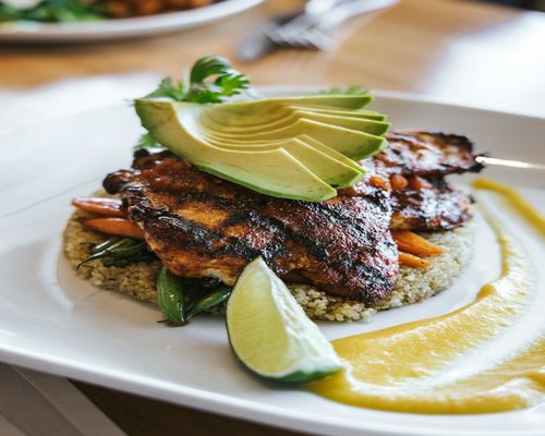 A freshly grilled fish fillet served with sliced avocados on a white plate